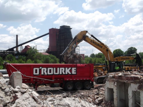 Excavator dropping building demolition debris into a dumpster